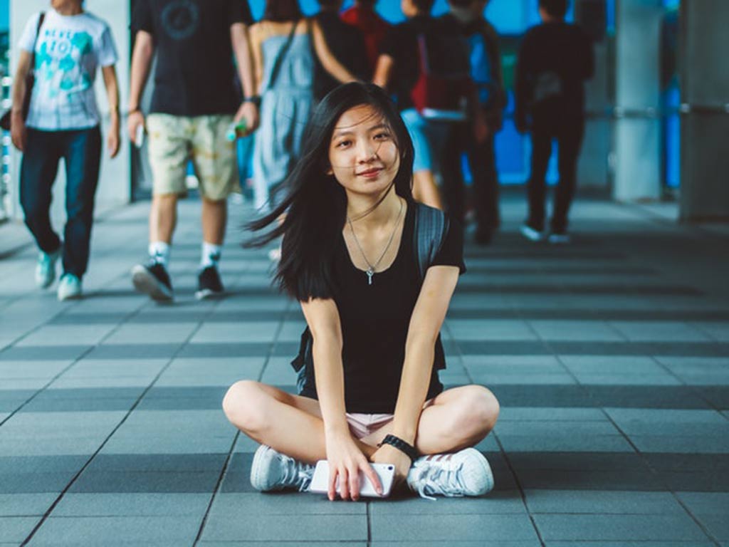 Female student sitting cross-legged in pedestrian traffic