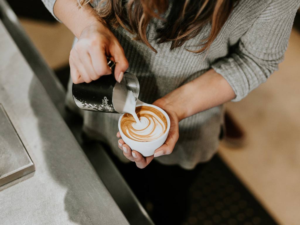 Female barista pouring milk into coffee – overhead shot