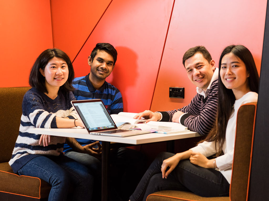 four international students at booth table with red wall behind
